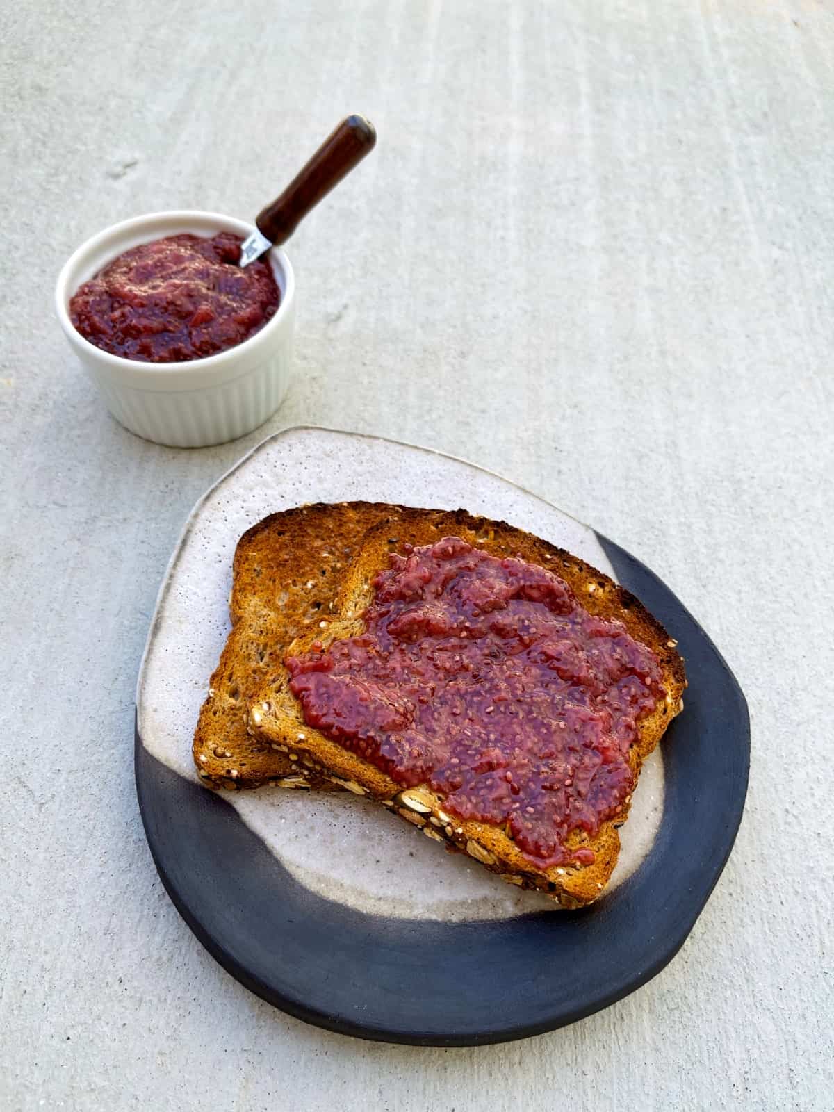 Strawberry chia jam on toast with small white ramekin of jam in the background.