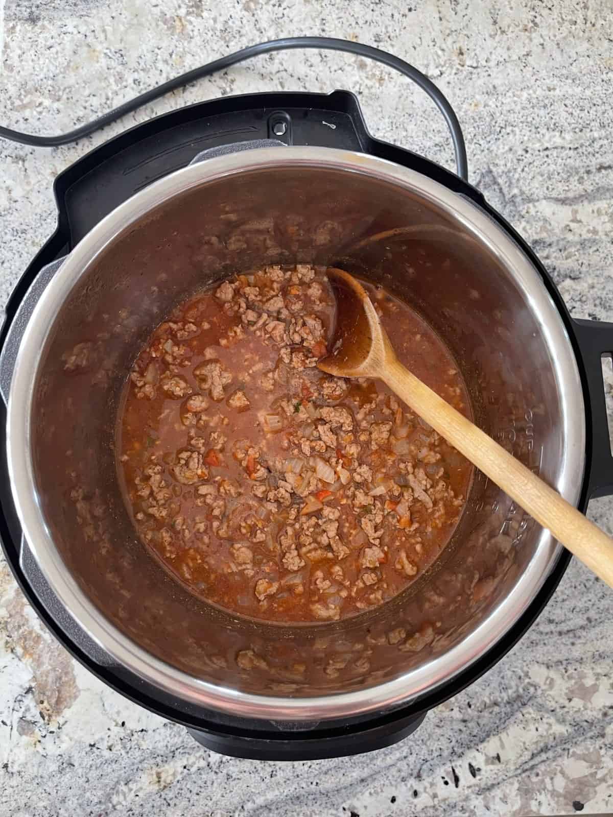 Sauteeing ground turkey, salsa and spices in Instant Pot with wooden spoon.