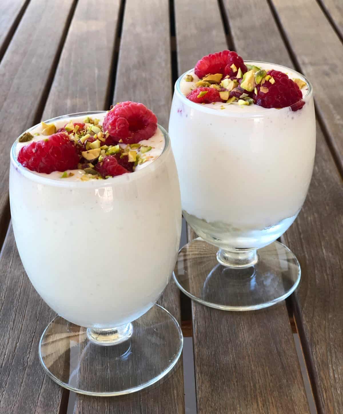 Two small glasses filled with cheesecake dessert and topped with fresh raspberries and chopped pistachios.