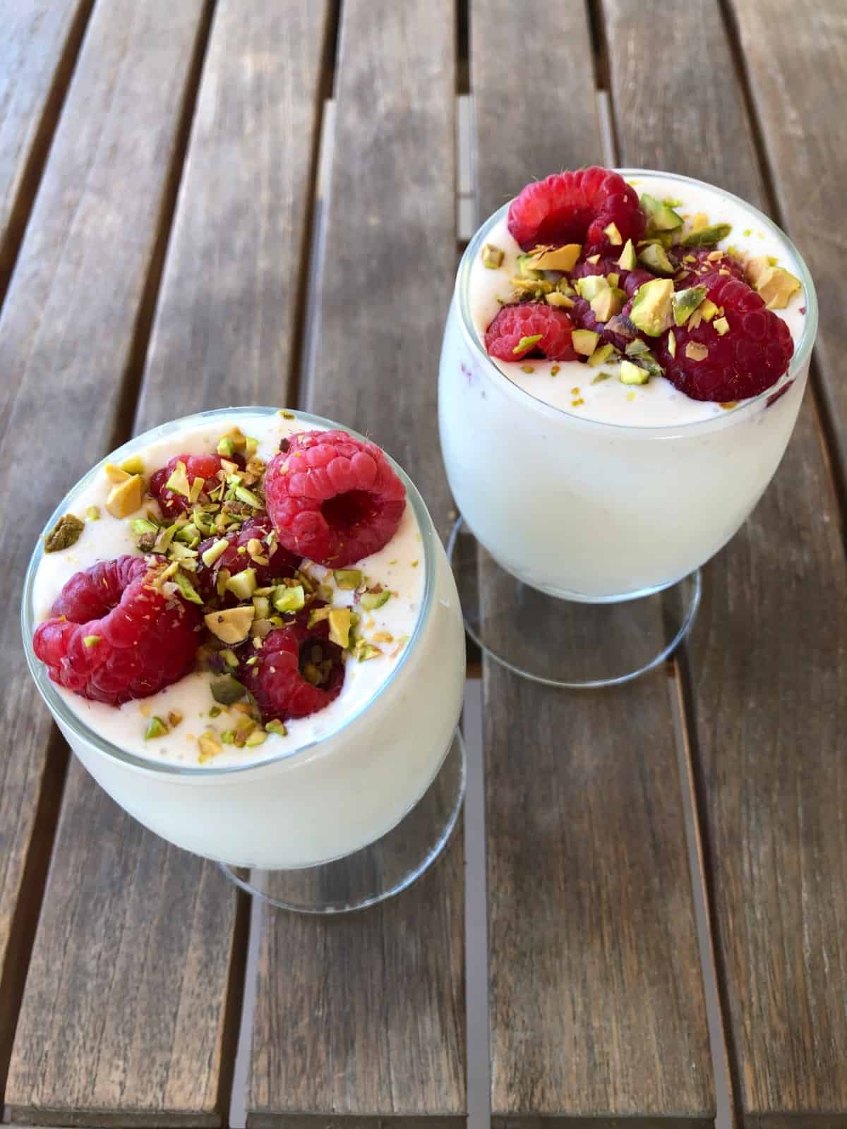 No-bake cheese cake cups topped with fresh raspberries and chopped pistachios.