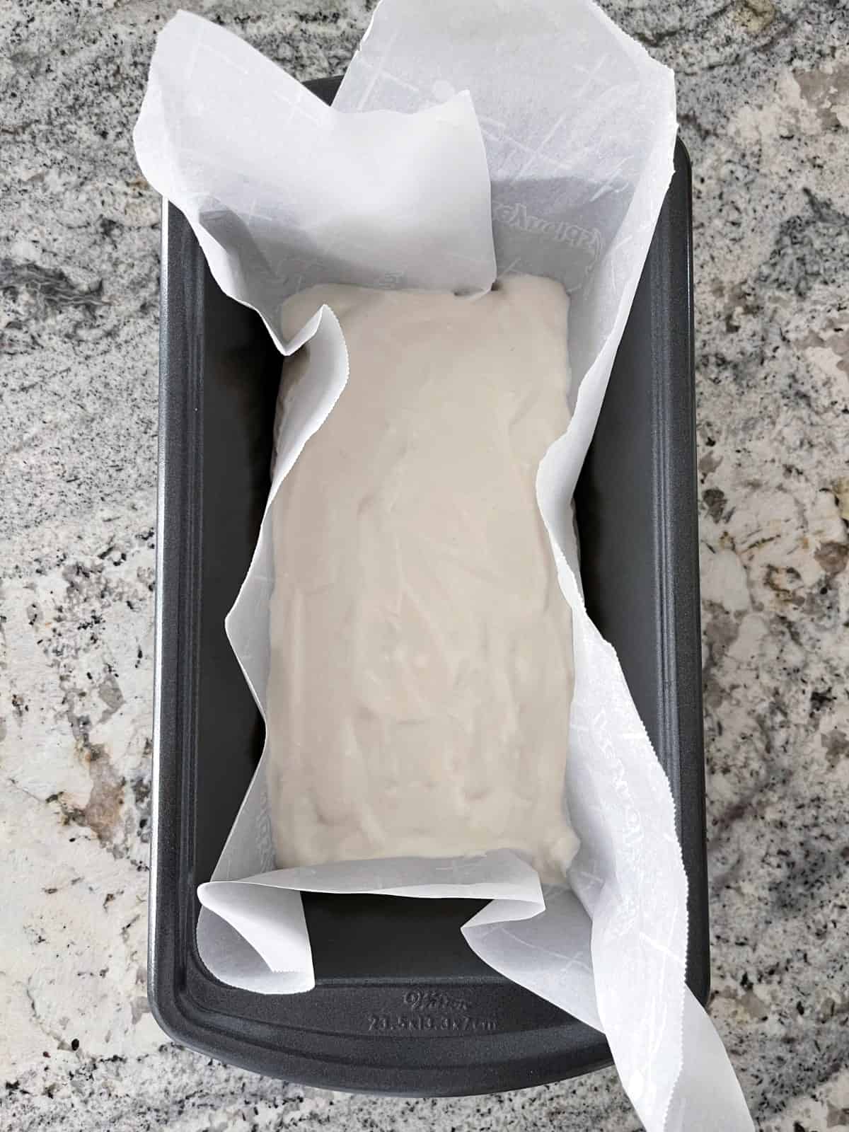 Layer of sweetened Greek yogurt in parchment paper lined loaf pan on granite counter.