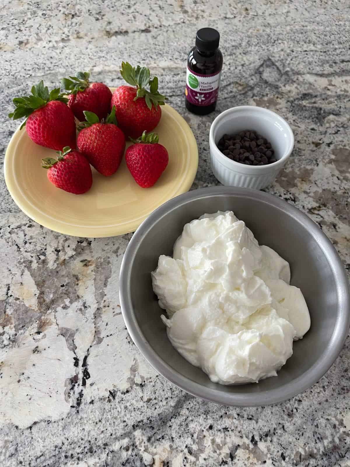 Ingredients for making frozen yogurt bark - including fresh strawberries, Greek yogurt, mini chocolate chips and vanilla extract.