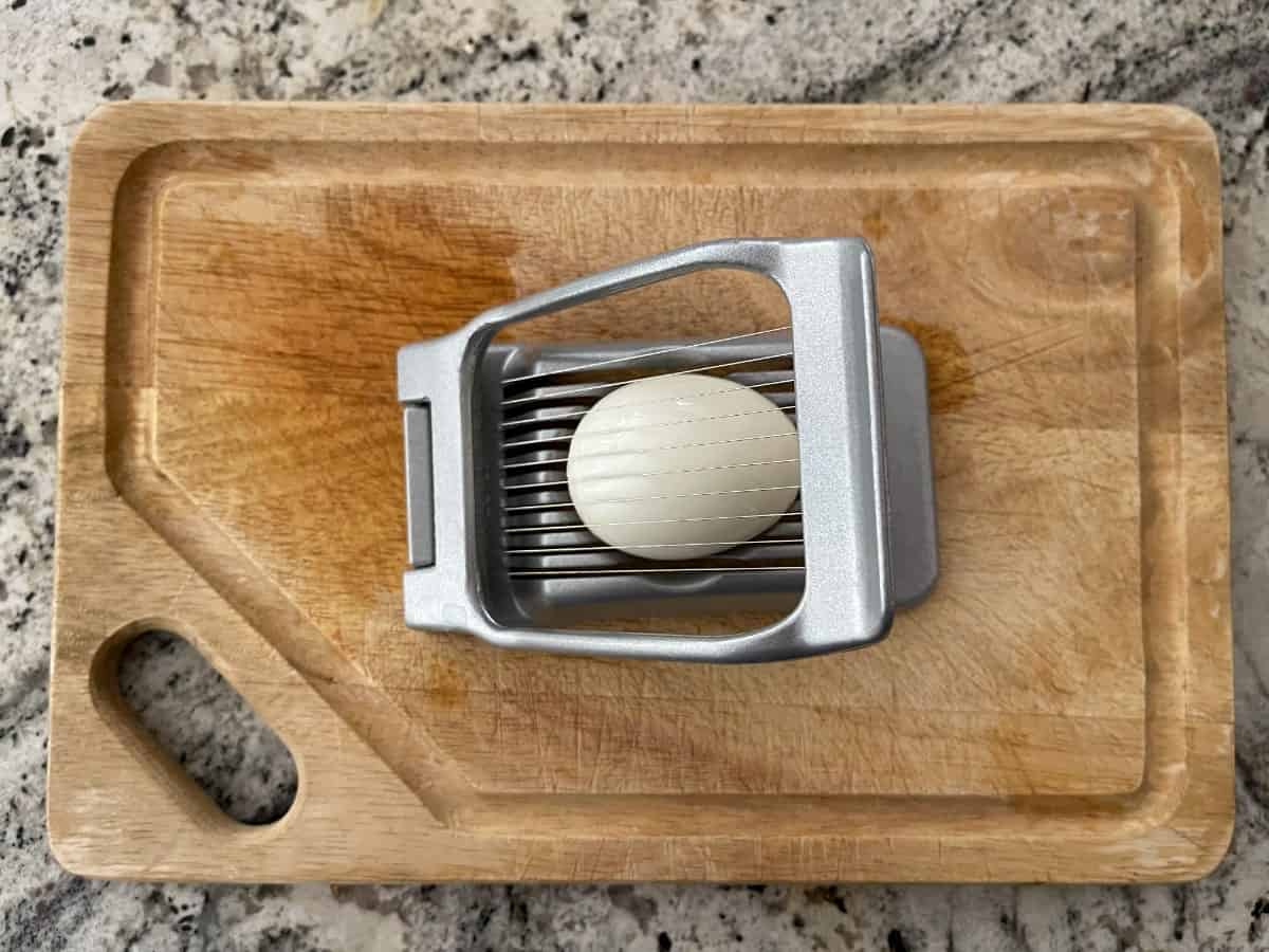 Slicing hard boiled egg with egg slicer on wood cutting board.