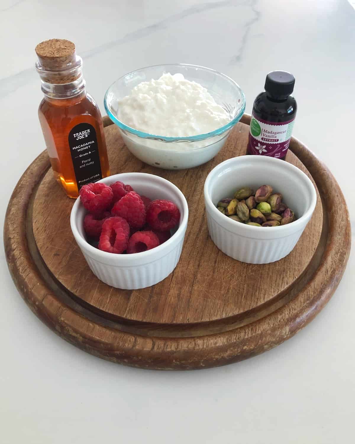Ingredients for making no-bake cheesecake cups, including honey, cottage cheese, vanilla extract, fresh raspberries and pistachios.