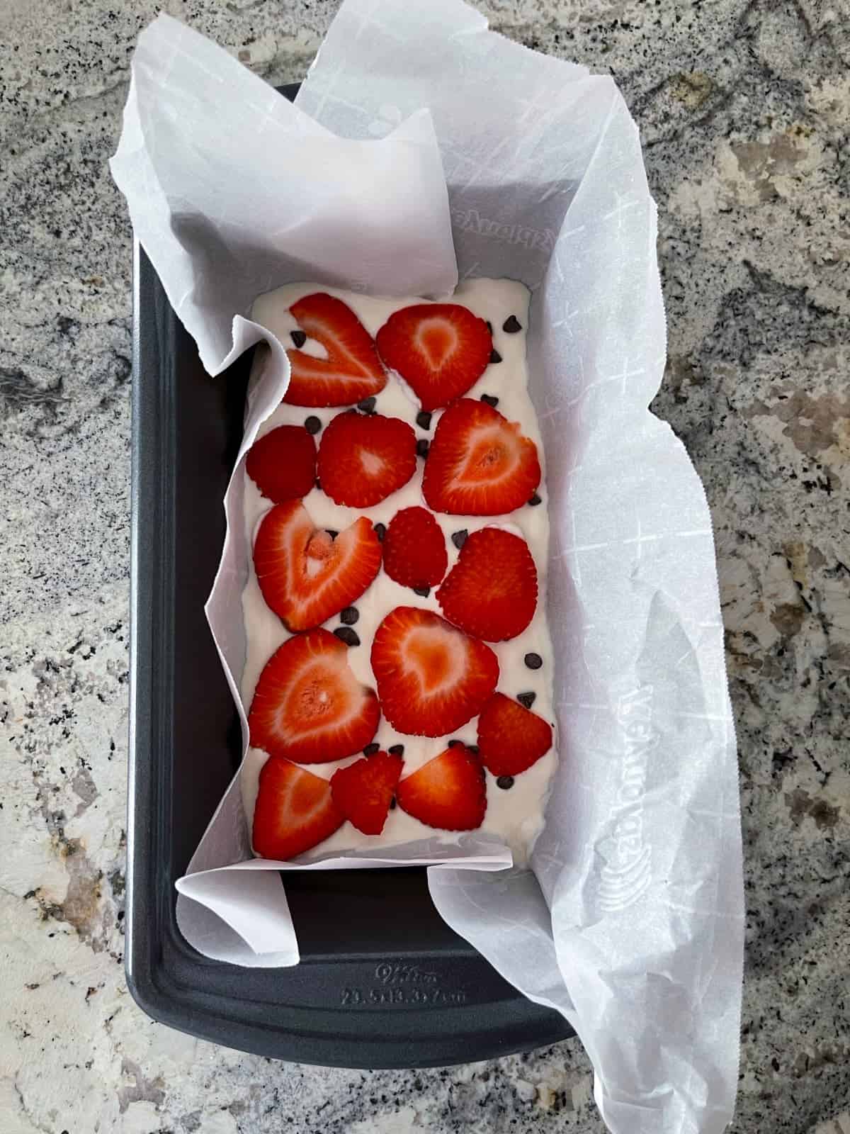 Layering sliced strawberries and chocolate chips over sweetened Greek yogurt in parchment-lined loaf pan.