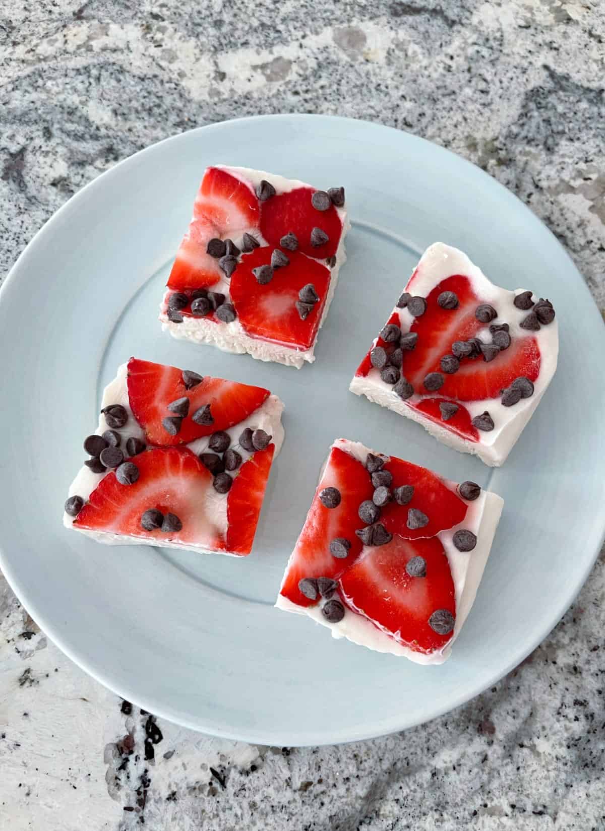 Four pieces Strawberry Chocolate Chip Frozen Greek Yogurt Bark on blue plate from above.