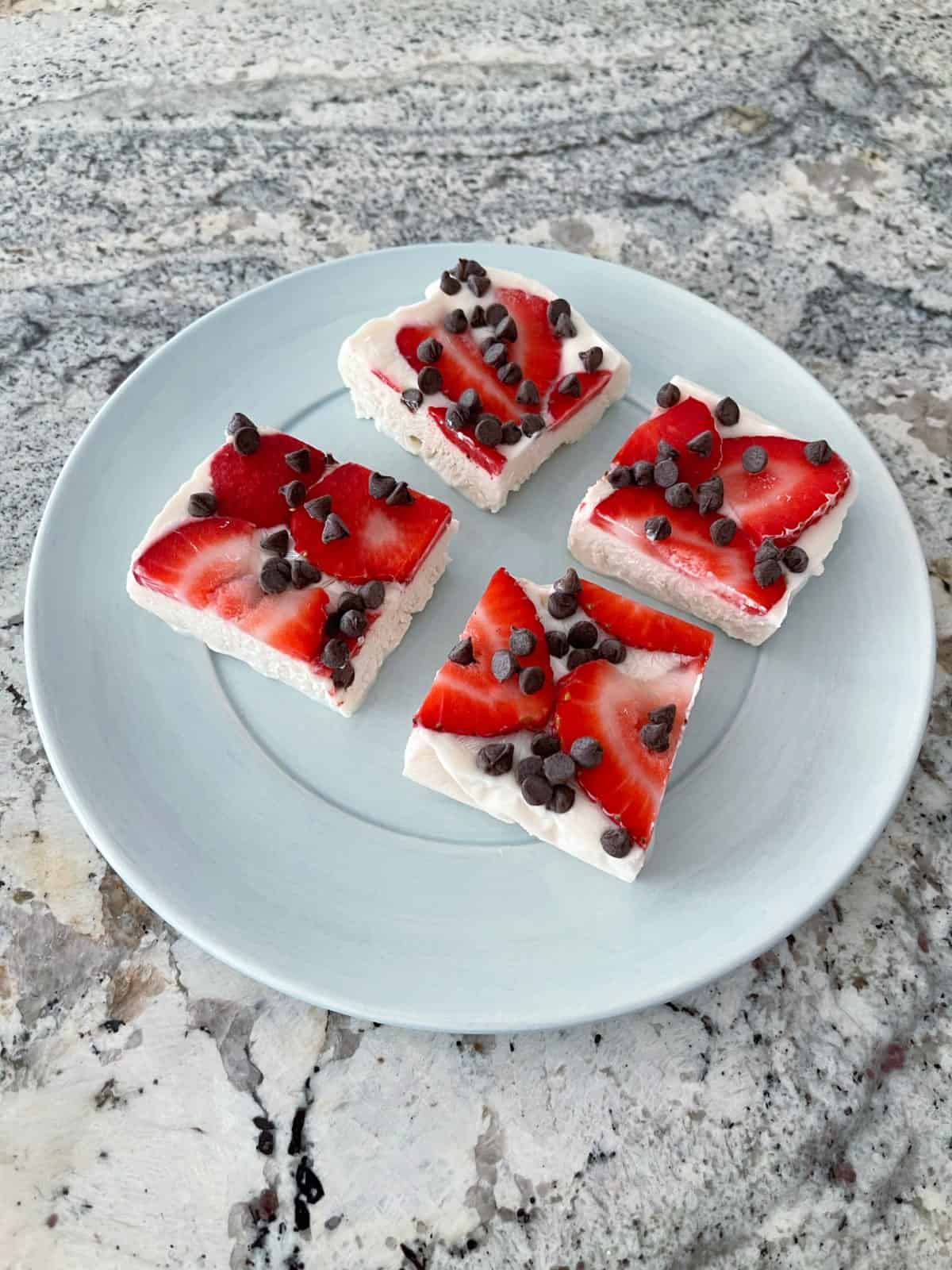 Four slices strawberry chocolate chip greek yogurt bark frozen dessert on small blue plate.