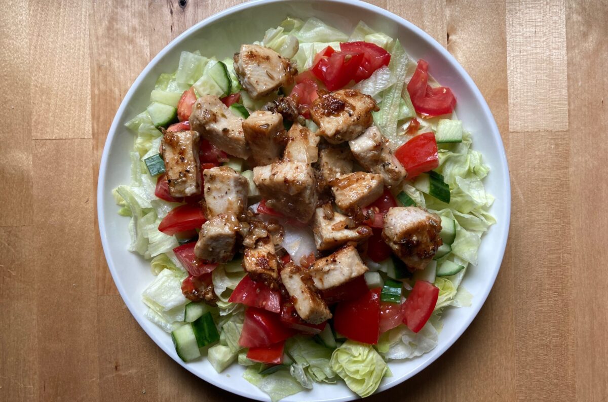 Plate of chopped lettuce, cucumber and tomato topped with fresh cooked chicken breast pieces.