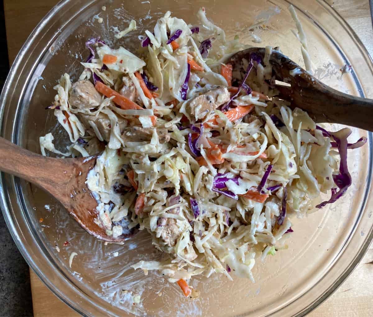 Mixing shredded chicken, cole slaw mix and caesar dressing in mixing bowl with wooden spoons.