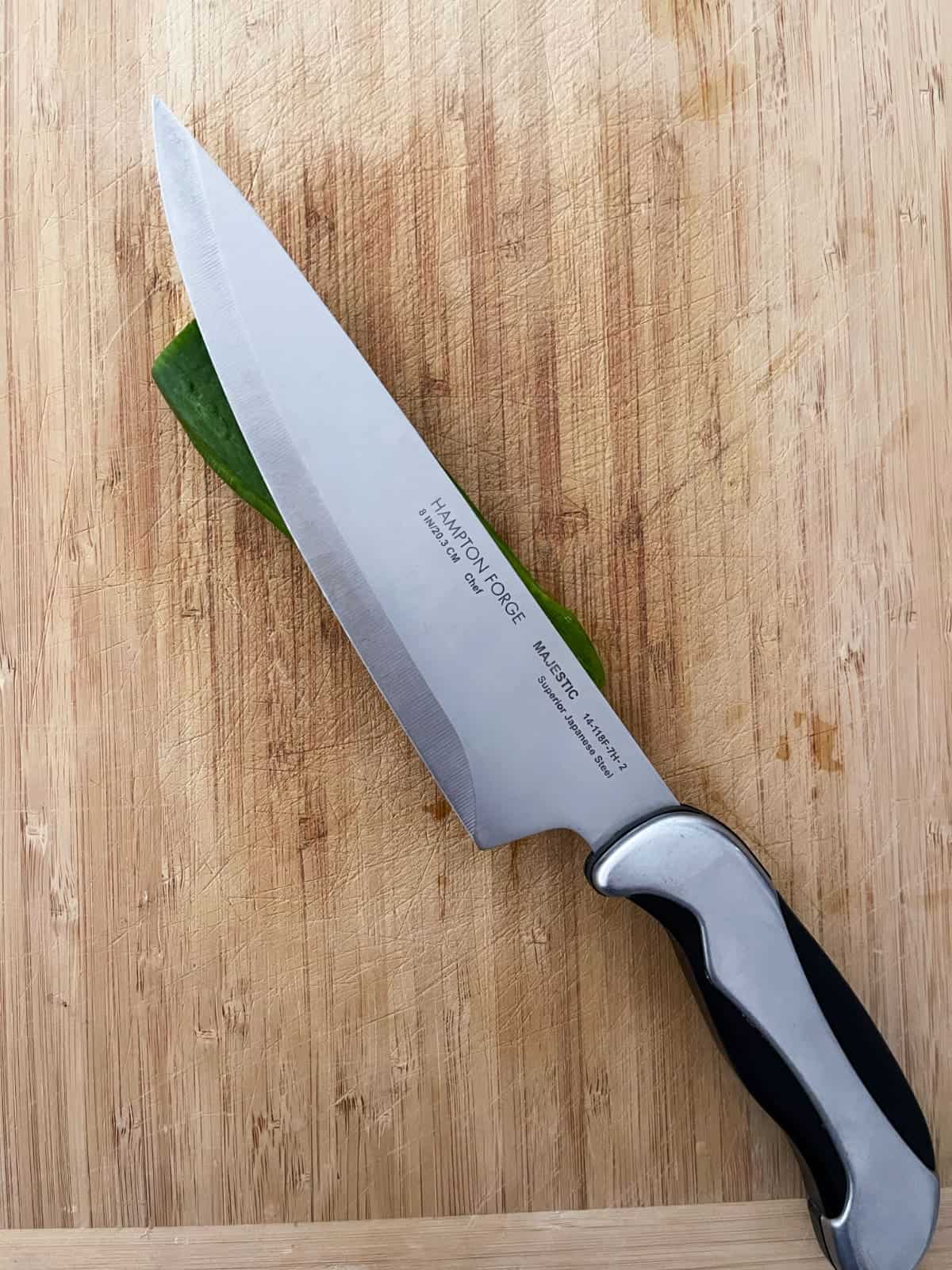 Chef knife on top of mini cucumber on wooden cutting board.