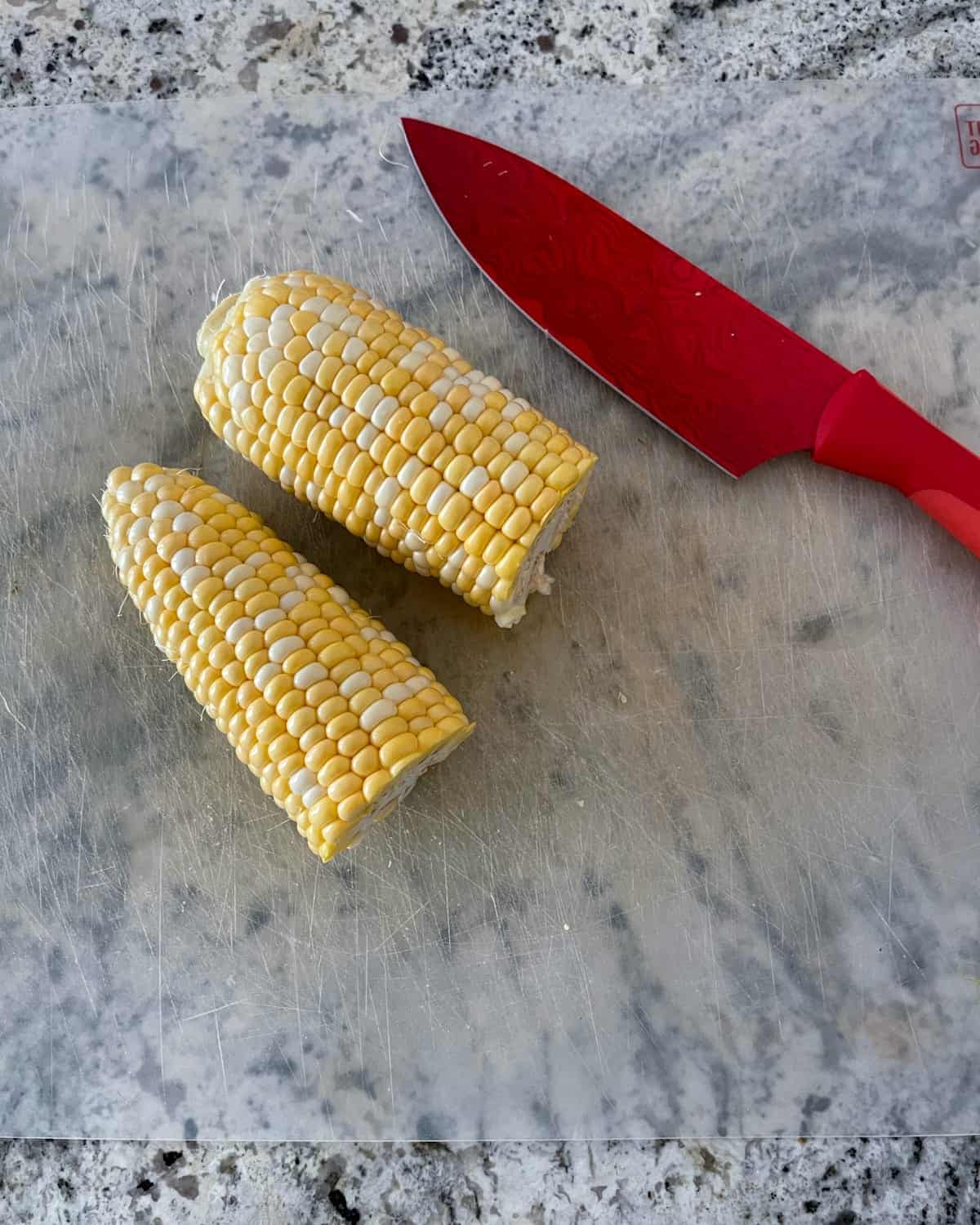 Corn cob cut in half with red knife.