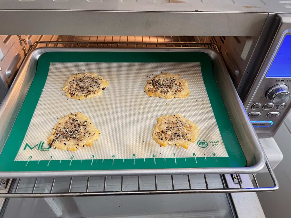 Baking everything bagel seasoned Parmesan cheese crisps on baking pan in toaster oven.