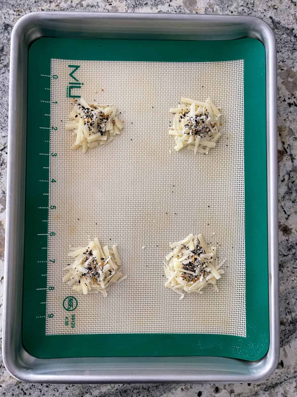 Shredded Parmesan cheese topped with everything bagel seasoning on silicone lined baking sheet.