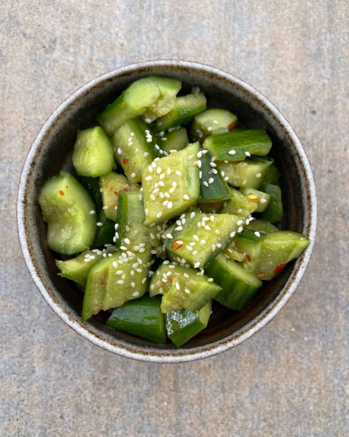 Chili spiced cucumber salad topped with toasted sesame seeds in ceramic bowl.