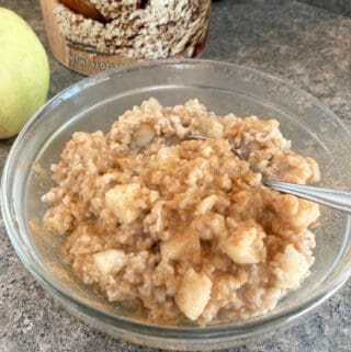 clear glass bowl with apple studded apple oatmeal with apple & container of oats in background