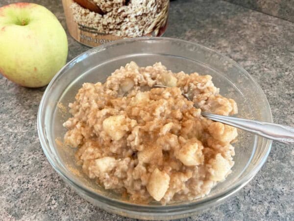 clear glass bowl with apple studded apple oatmeal with apple & container of oats in background