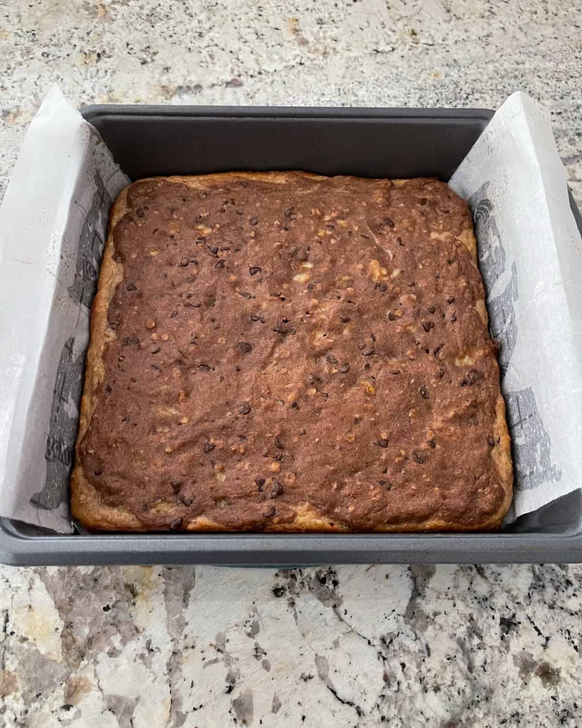 Banana bread brownies in parchment lined baking pan on granite counter top.