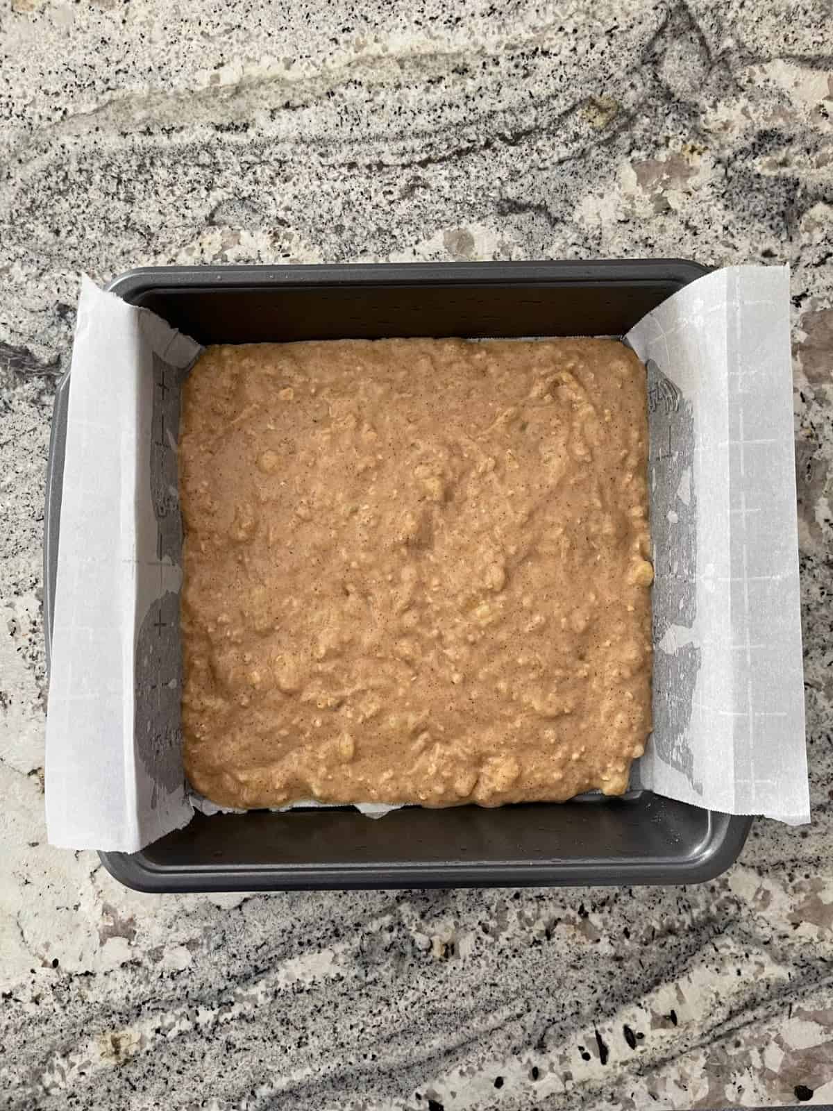 Unbaked banana bread batter in parchment lined baking pan on granite counter.