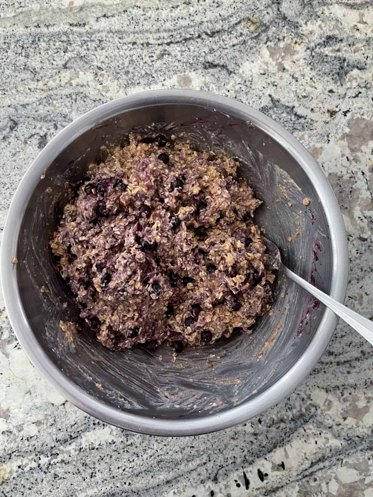 Mixing the blueberry banana oat batter in stainless bowl on granite counter.