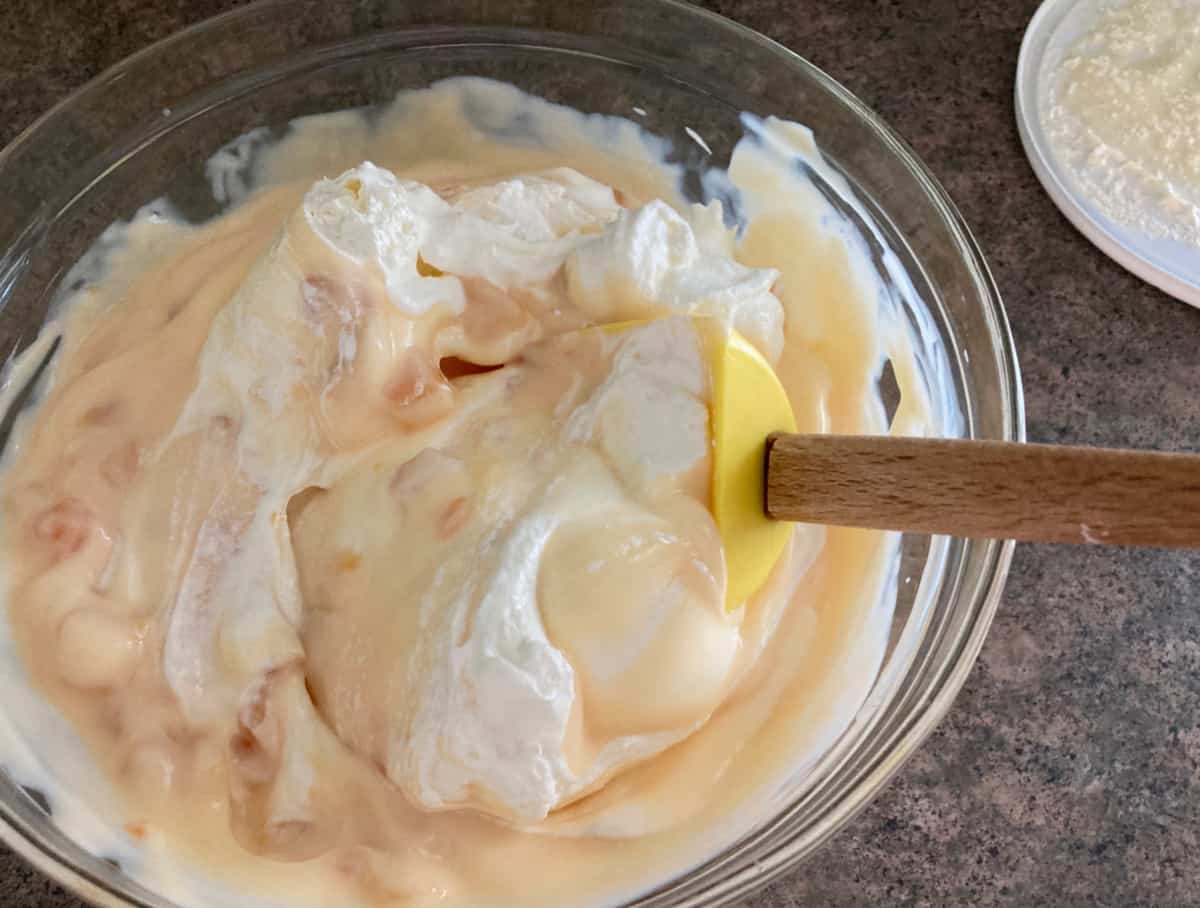 Mixing peaches, yogurt and lite whipped topping in glass bowl with spatula.