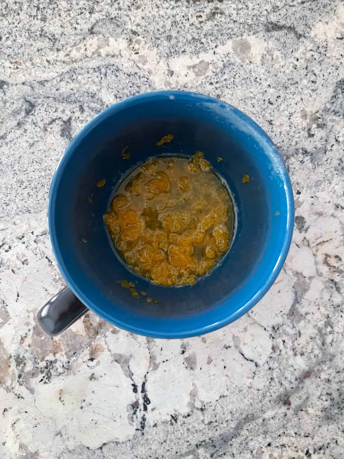 Mashed mandarin oranges in juice in blue mug on granite.
