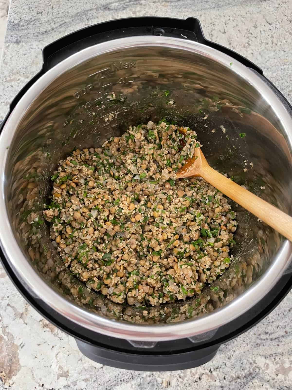 Stirring chopped cilantro and parsley into Mediterranean lentils with quinoa in Instant Pot.