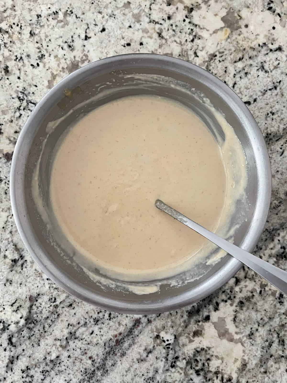 Mixing tahini dressing in stainless mixing bowl with spoon.