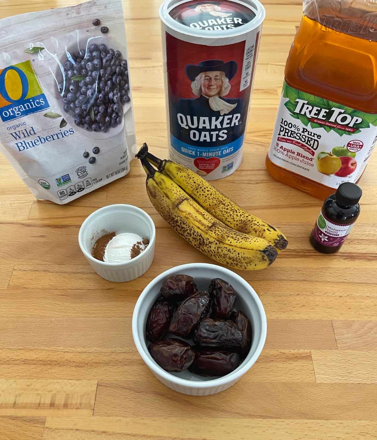 Ingredients for making baked oat squares including frozen blueberries, ripe bananas, dates, oats, apple juice and vanilla.