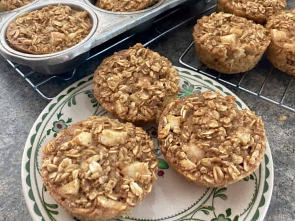 3 individual apple baked oatmeal muffin cups on patterned plate with muffin tin in background