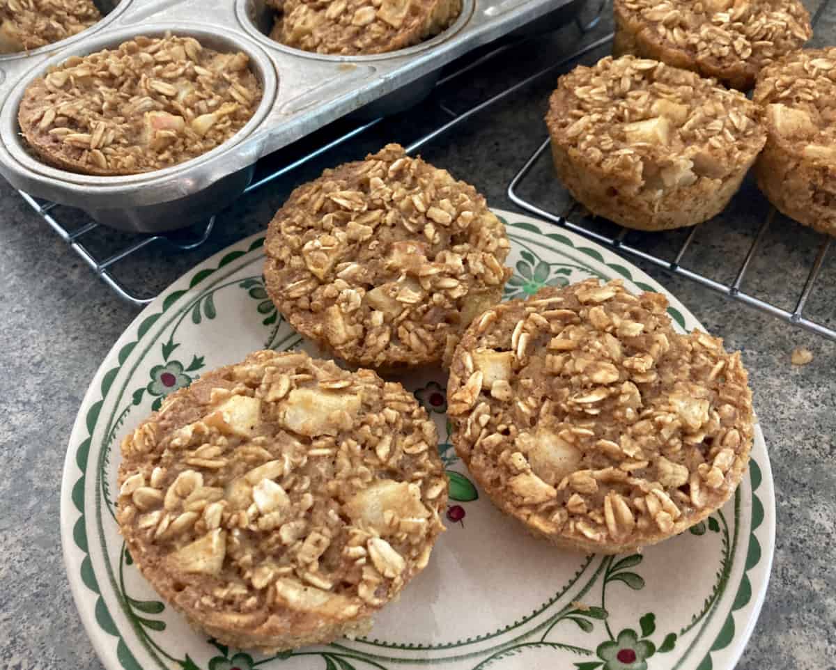 3 individual apple baked oatmeal muffin cups on patterned plate with muffin tin in background