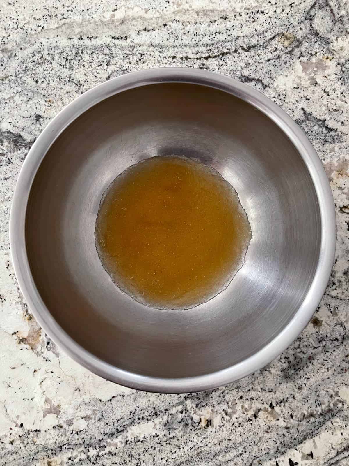 Blooming gelatin in apple juice in mixing bowl on granite.