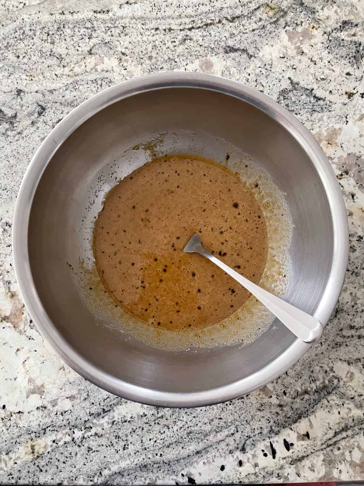 Stirring oil, eggs, Truvia, vanilla, espresso powder and salt in mixing bowl on granite counter.