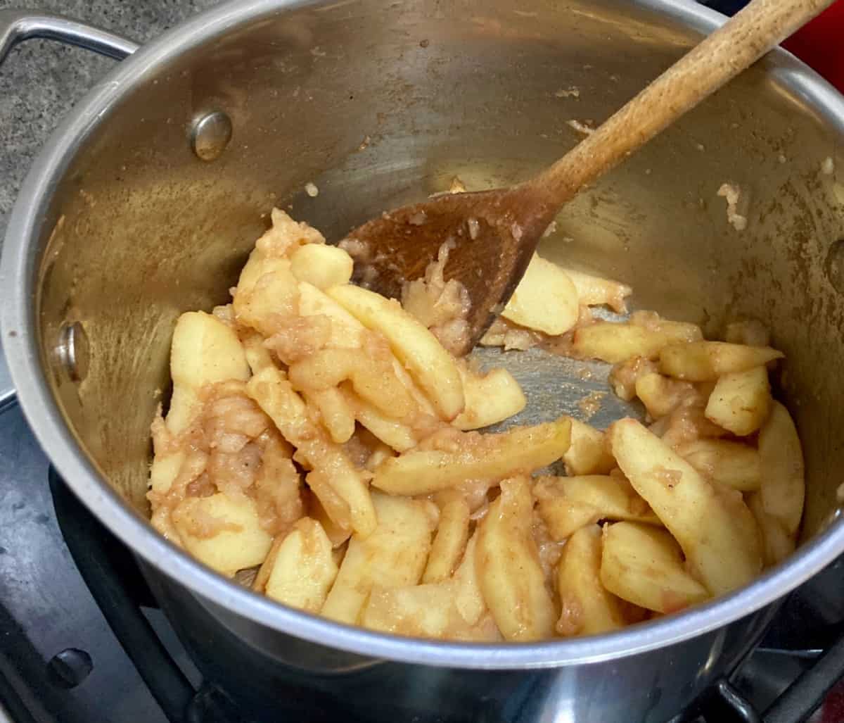 Cooking apples and cinnamon in saucepan with wooden spoon.