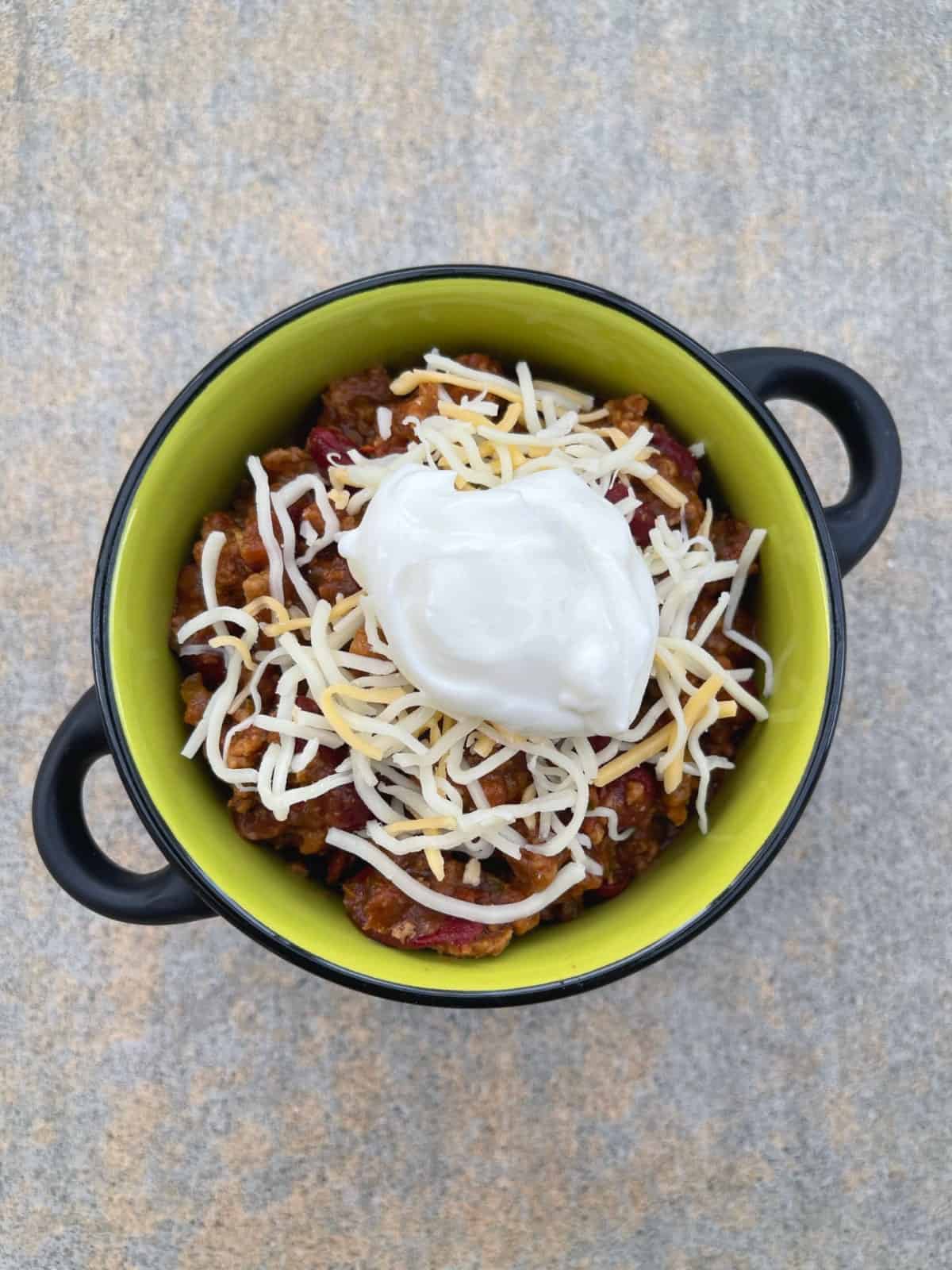 Meatless Quorn chili in green crock topped with shredded cheese and lite sour cream from above.
