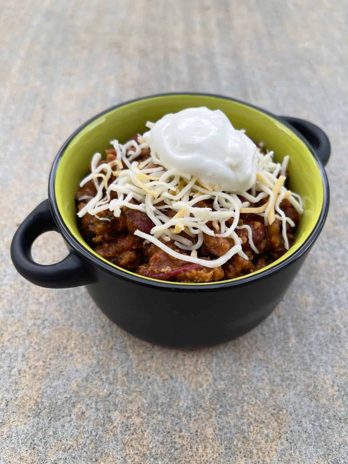 Meatless chili in green bowl with Greek yogurt and shredded cheese.