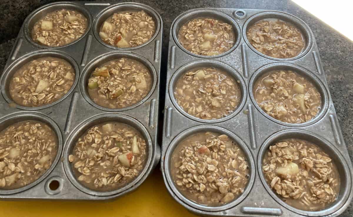 Two 6-cup muffin tins filled with unbaked apple pie oatmeal batter.