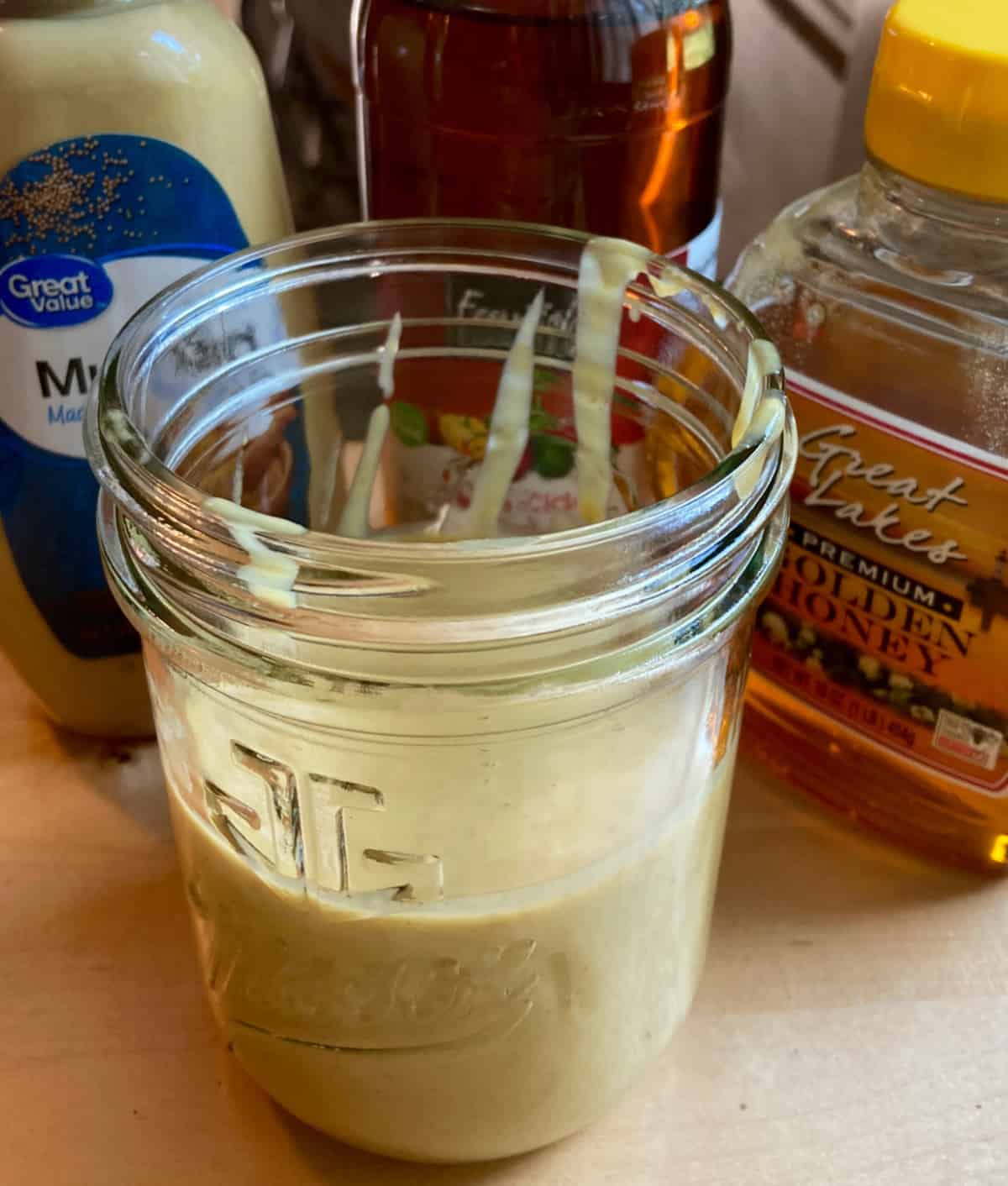 Glass jar with homemade honey mustard dressing and bottle of Dijon mustard and honey in the background.