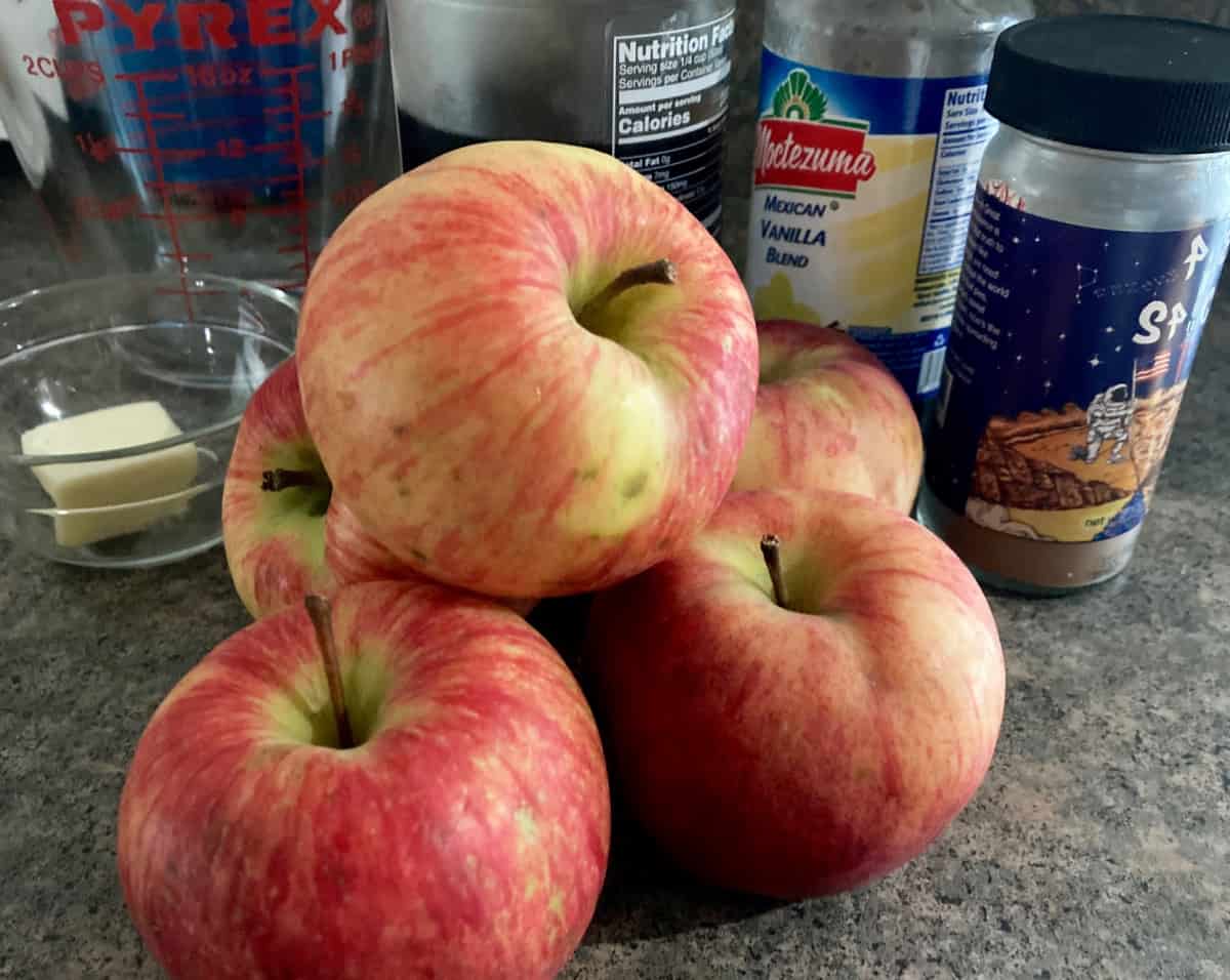Ingredients for making cinnamon apples, including whole apples, butter, vanilla and spices.