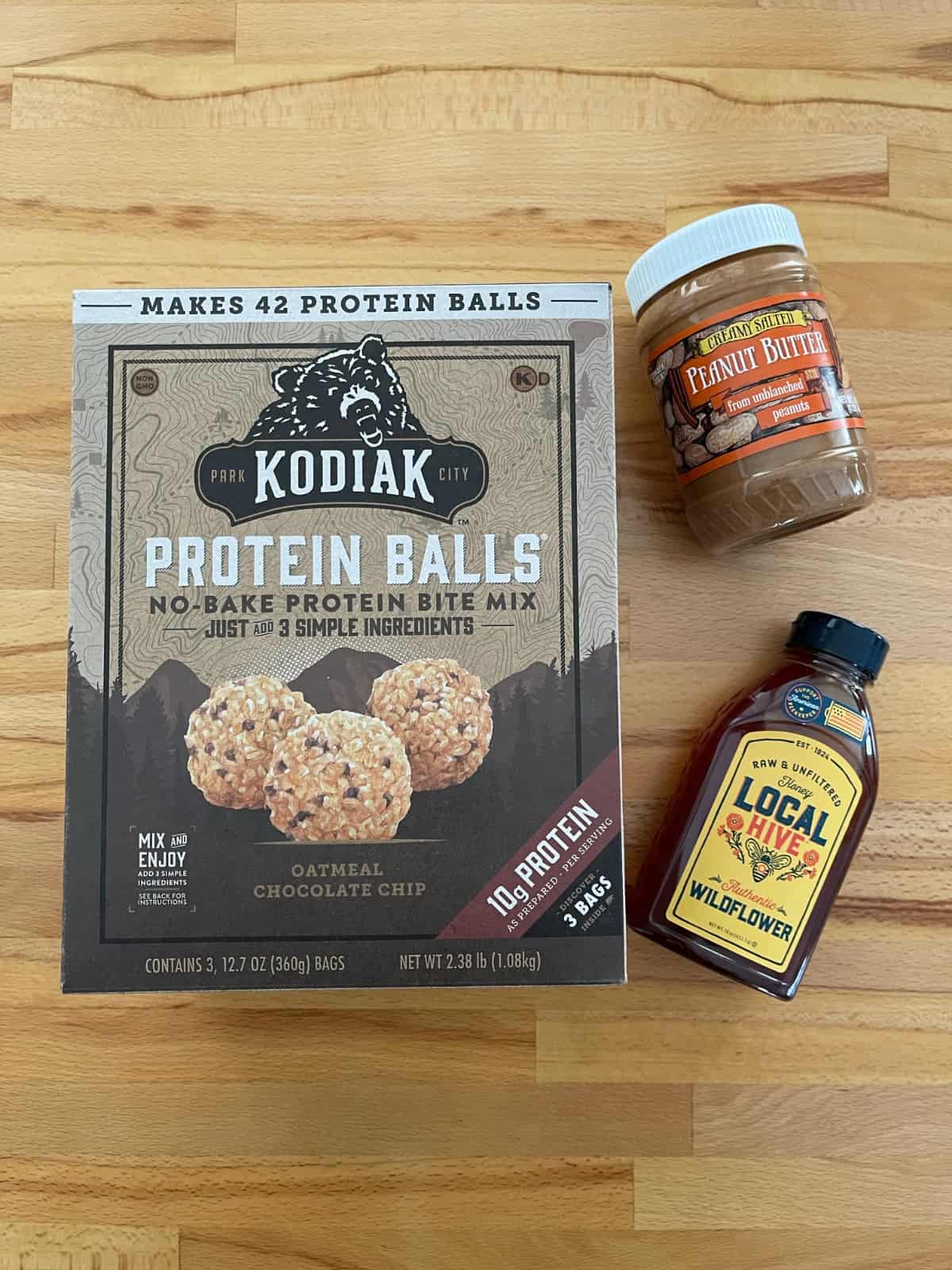 Box of Kodiak no-bake protein bite mix, honey and peanut butter on wooden table.