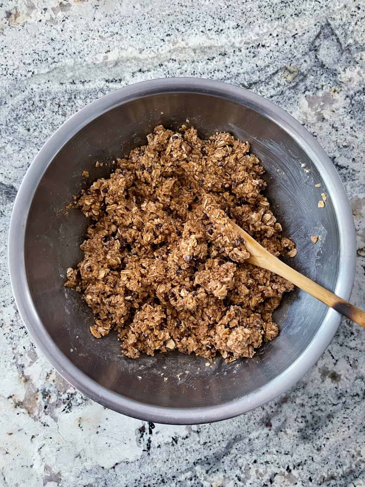 Stirring Kodiak no-bake oatmeal chocolate chip protein bite mix with honey, water and peanut butter in mixing bowl with wooden spoon.