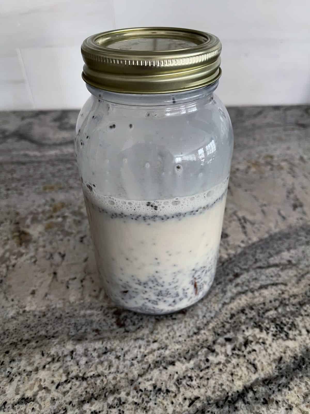 Covered mason jar containing almond milk, chia seeds and dates on granite counter.