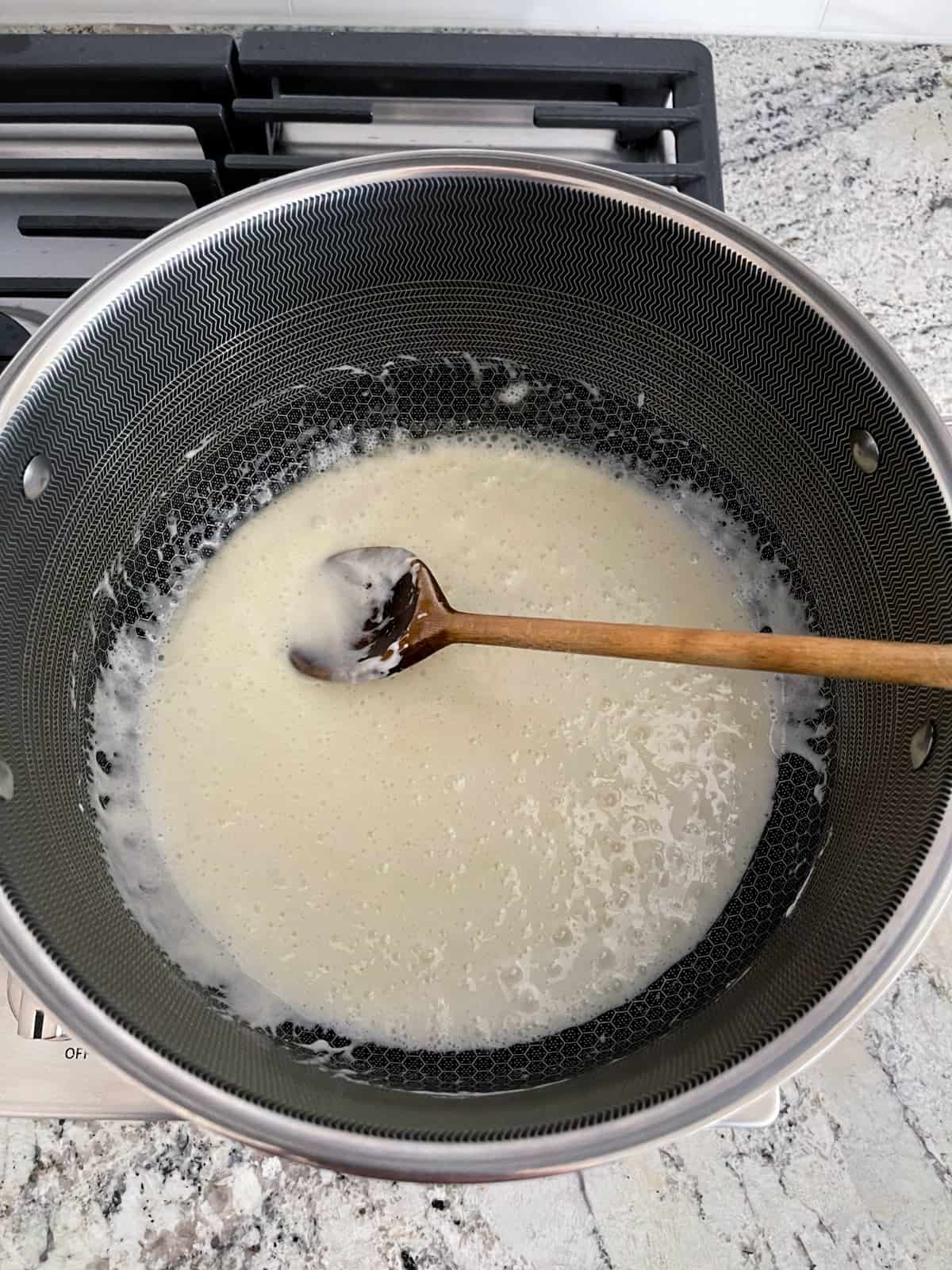 Stirring melted marshmallows in large saucepan with wooden spoon on stovetop.