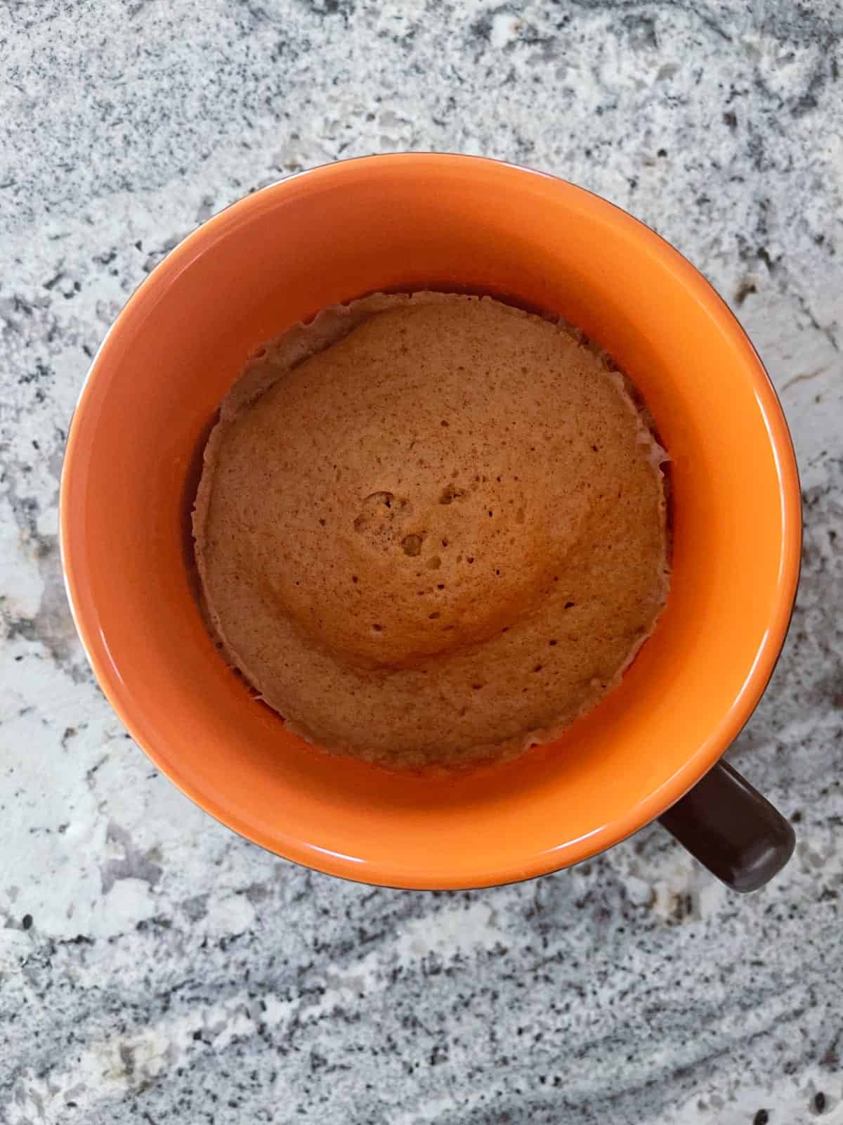 Microwave gingerbread in orange mug on granite counter.