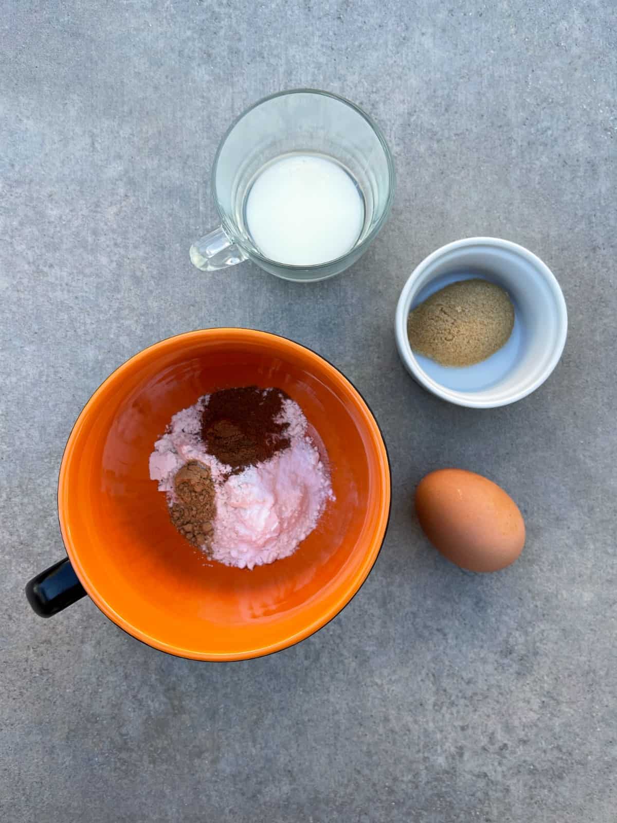 Ingredients for making gingerbread mug including milk, Truvia brown sugar blend, egg, flour and spices in orange mug.