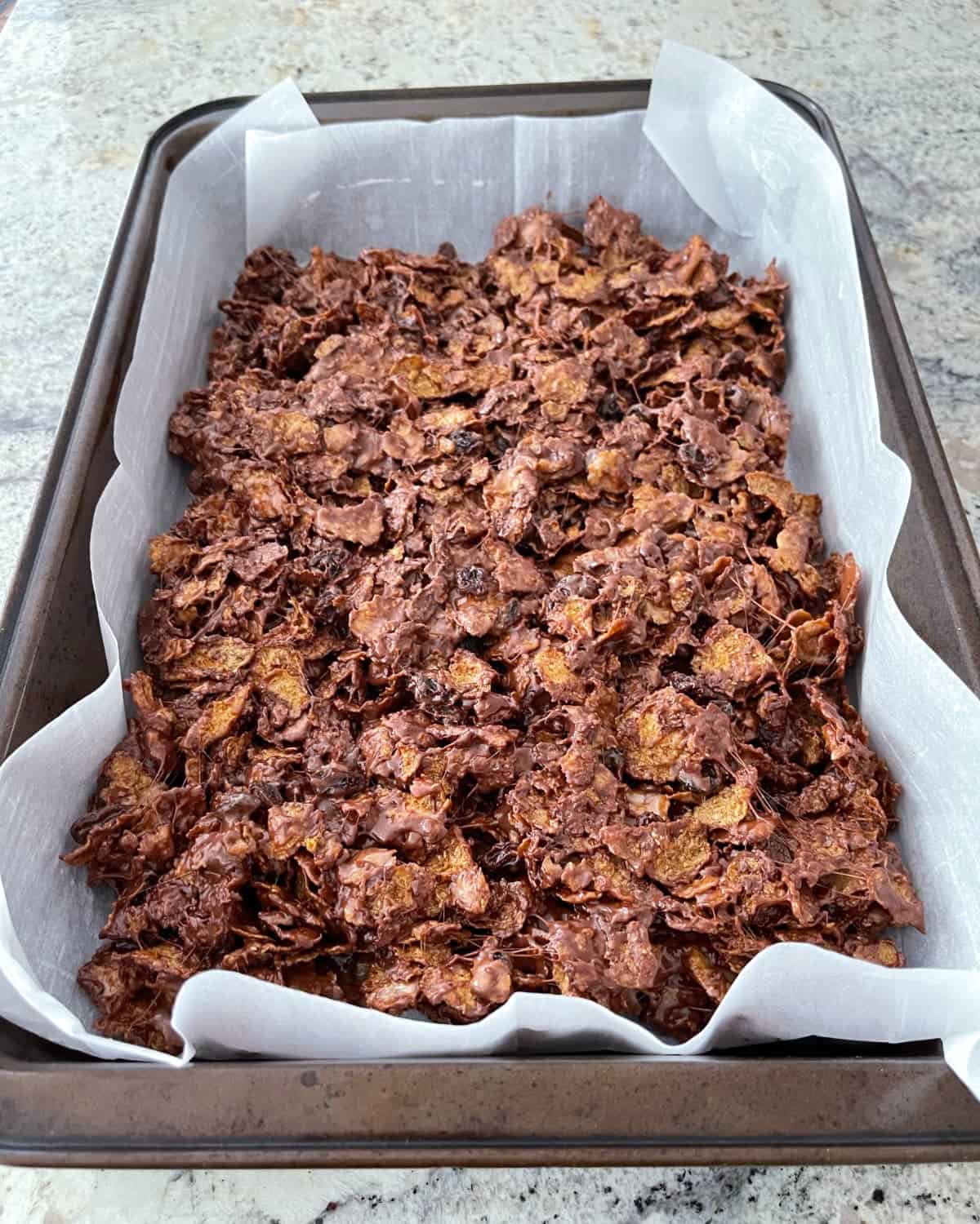 Chocolate Raisin Bran cereal bars in parchment lined baking pan.