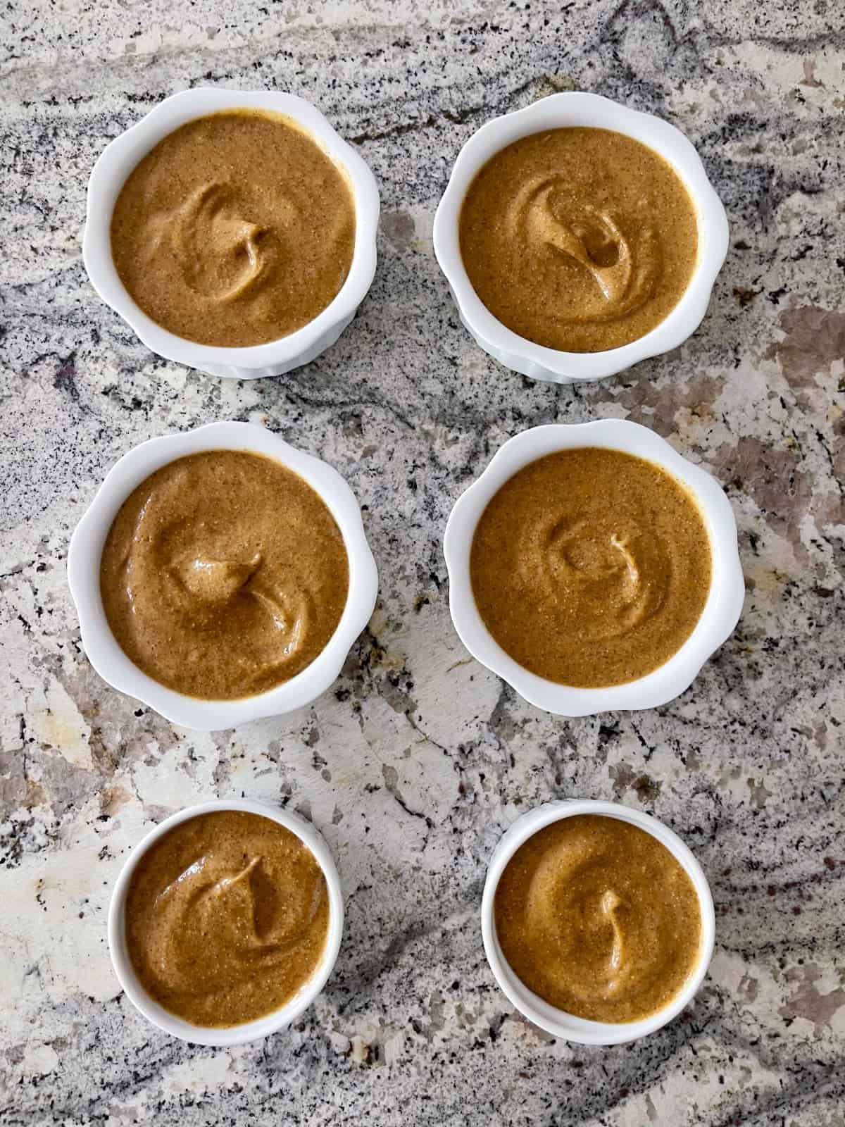 Pumpkin pie chia pudding in six small white ramekins on granite counter from above.
