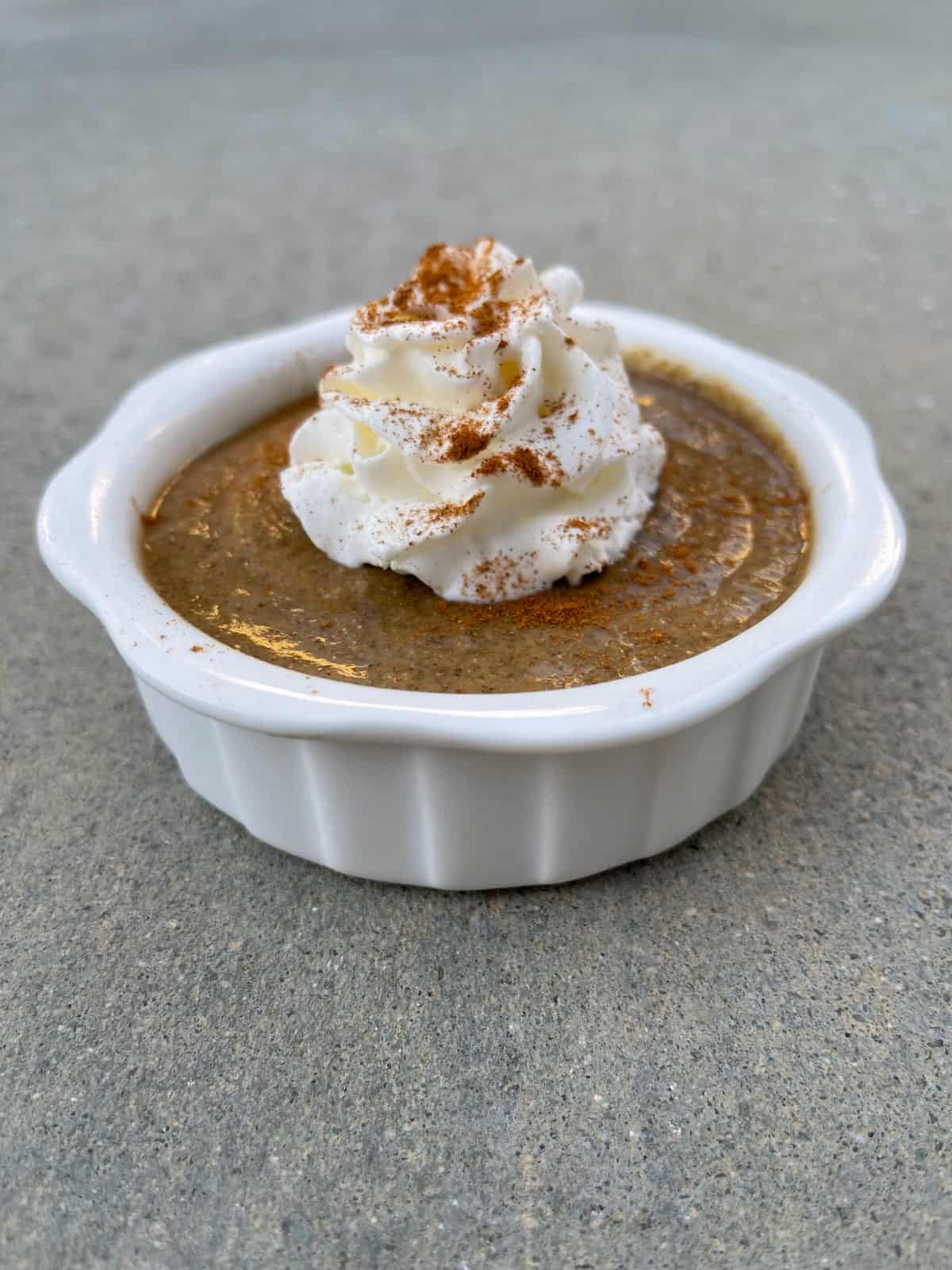 Pumpkin pie chia pudding topped with whipped cream and sprinkle of cinnamon in white ramekin.