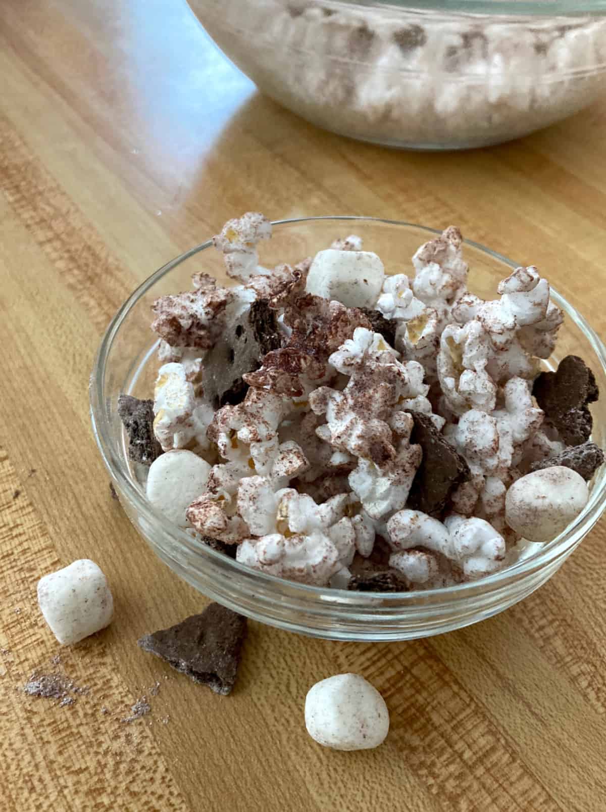 S'mores popcorn with crushed chocolate graham crackers and mini marshmallows in small glass bowl.