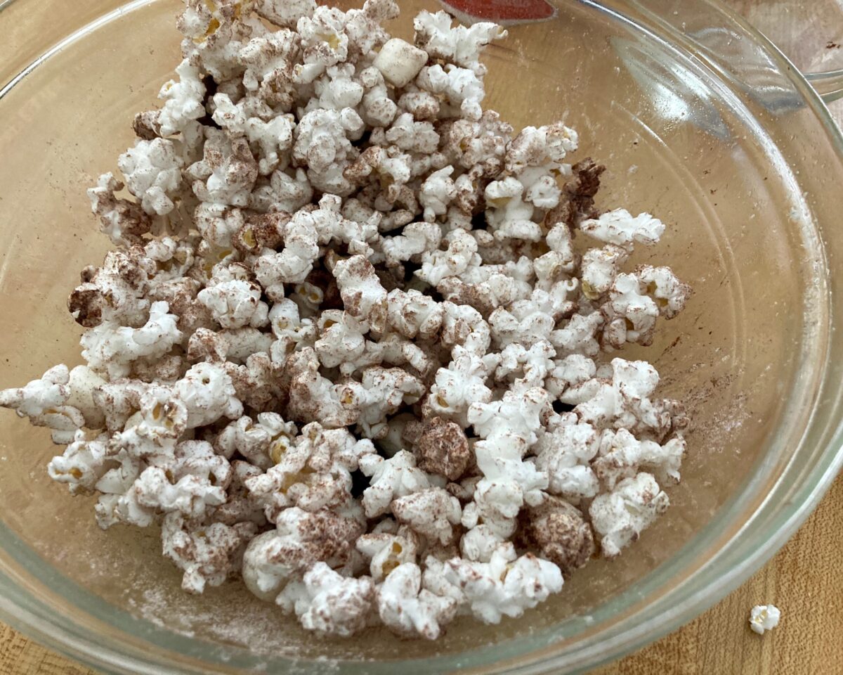 Tossing s'mores popcorn with crushed chocolate graham crackers and mini marshmallows.