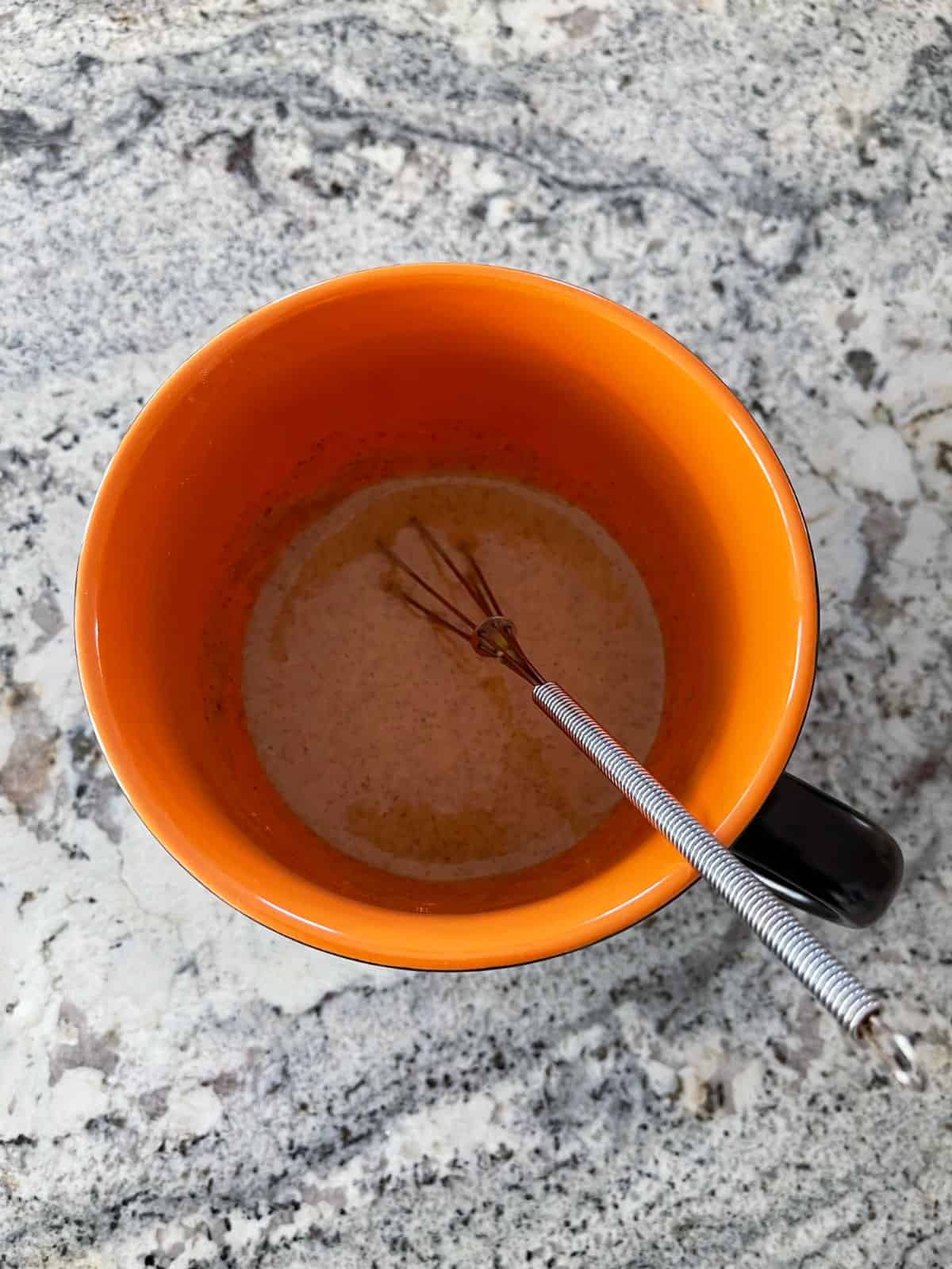 Whisking gingerbread batter in orange mug.